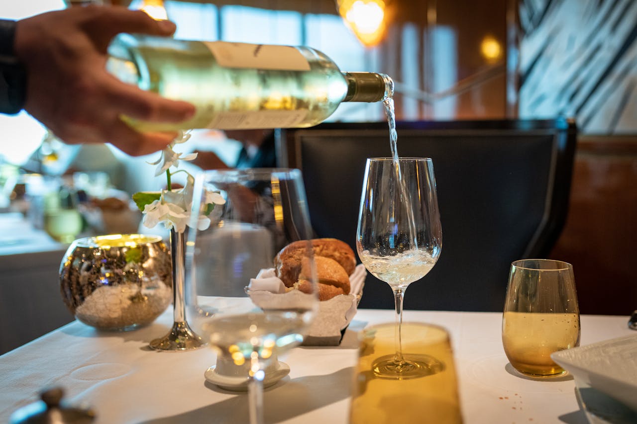 Close-up of wine being poured in a glass on a fine dining table setting.